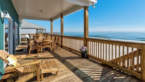 A wooden deck with outdoor furniture, a railing, and a view of the ocean.