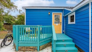 A small blue house with a yellow door, a porch with a green railing, and a bicycle parked outside.