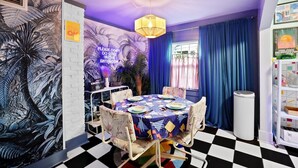 A room with a checkered floor, a table set for dining, a mural with palm trees, and a sign that says "PLEASE DON'T DO COKE IN THE BATHROOM".