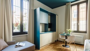 A modern room with a sofa, a dining table with chairs, a kitchen area, and large windows. - Bright Ground-floor Studio in Milan (Milan)