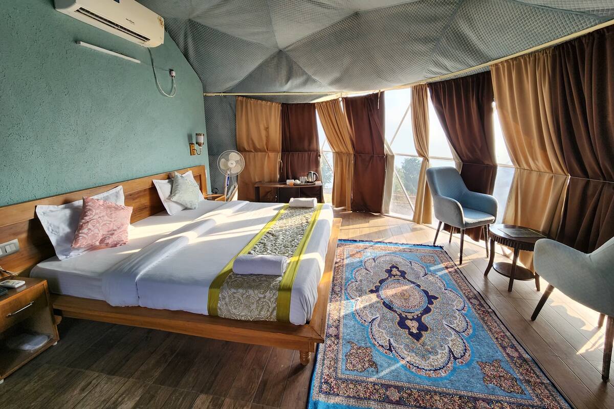A hotel room with a bed, a desk, a chair, and a large window with curtains.