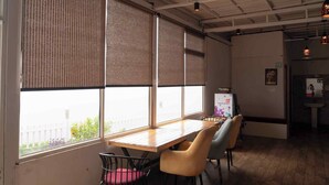 Una habitación con una mesa de madera, sillas, ventanas amplias con persianas y un techo con vigas a la vista.