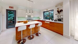 A modern kitchen with a central island, bar stools, a stove, and a window with a view of greenery. - Charming house in Golders Green - Pass the Keys (London)