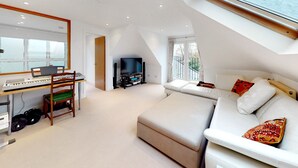 A modern loft bedroom with a large skylight, a sofa bed, a desk with a computer and speakers, and a TV. - Charming house in Golders Green - Pass the Keys (London)