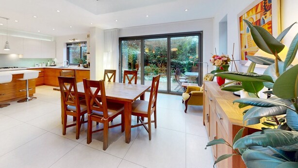 A modern kitchen with a central island, a dining area with wooden chairs, and a large sliding glass door leading to a garden. - Charming house in Golders Green - Pass the Keys (London)