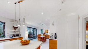A modern kitchen with a central island, wooden cabinets, and a dining area with a table and chairs. - Charming house in Golders Green - Pass the Keys (London)