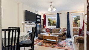 A living room with a fireplace, a television, a bookshelf, and a window with curtains.
