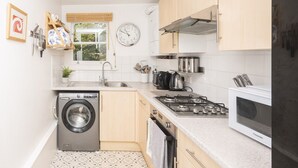 A compact kitchen with a washing machine, stove, microwave, and a clock on the wall. - Brockley Victorian apartment train links London - Pass the Keys (London)