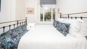 A bedroom with a large bed, a window with a view of greenery, and a framed picture on the wall. - Brockley Victorian apartment train links London - Pass the Keys (London)