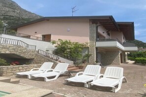 Un edificio con fachada de piedra, un balcón y una zona de piscina con sillas de descanso blancas.