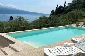 Une piscine rectangulaire à l’eau d’un bleu limpide, entourée d’une terrasse carrelée et de chaises longues blanches.