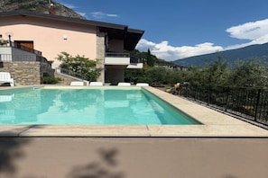 A swimming pool with a stone border, a white chair, and a black fence.