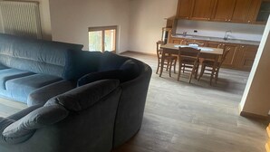 Una sala de estar con un sofá seccional gris, una zona de comedor con sillas de madera y una mesa, y una cocina con armarios de madera y una encimera.