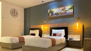 Una camera d'albergo moderna con due letti, una grande sveglia a parete, un quadro con vista sulla città e un comodino con telefono e caricabatterie.