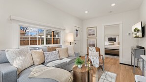A modern living room with a grey sofa, a coffee table, and a dining area with a table and chairs. - Chic Luxury Retreat – Old Town Carriage House (Fort Collins)