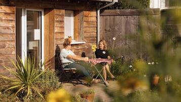 Eine Terrassengruppe im Freien mit Holzdeck, einem Tisch mit rot-weiß kariertem Tuch und Blumentöpfen.