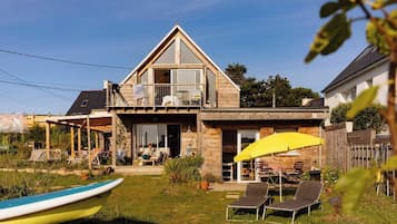 Une maison à deux étages avec un balcon, une terrasse dotée de mobilier d’extérieur et un bateau au premier plan.
