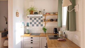 Kompakti keittiö, jossa on ruutukuviollinen välitila, puinen työtaso ja sisäänrakennettu liesi. Työtasolla on pesuallas, vedenkeitin ja ruukkukasvi.