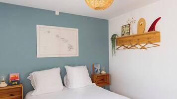 A bedroom with a bed, a map on the wall, a wooden shelf with surfboards, and a hanging plant.