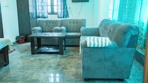 A living room with a sofa, a coffee table, and a television on the wall. - VJ Rooms (Bengaluru)