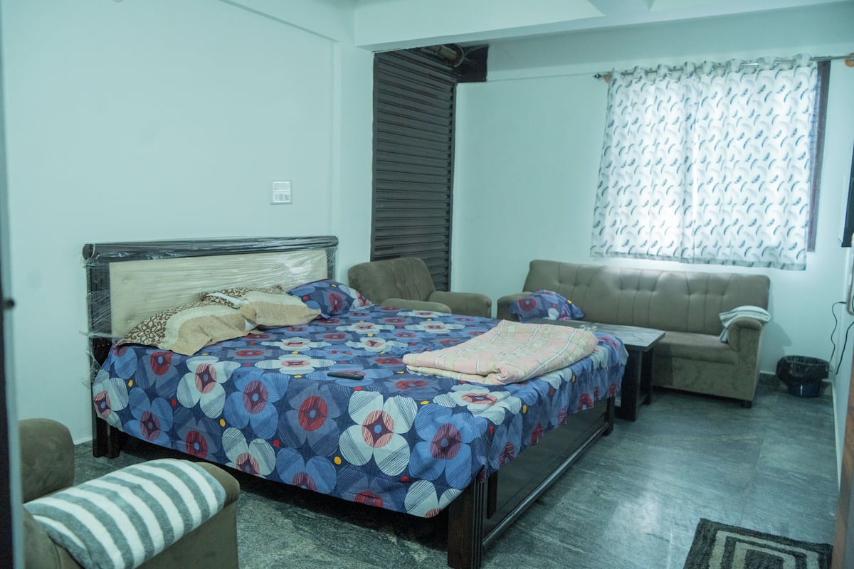 Quarto com cama, sofá e janela com cortinas.