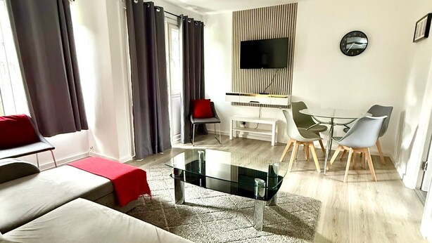 A modern living room with a glass coffee table, a sofa, a red chair, a dining area with a glass table and chairs, and a TV mounted on the wall. - Spacious 2 Bedroom flat with Balcony – 5 min to Kennington Tube, Central London (London)