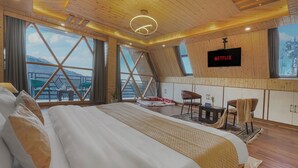 A modern hotel room with a large bed, a TV mounted on the wall, and a view of the mountains through large windows.