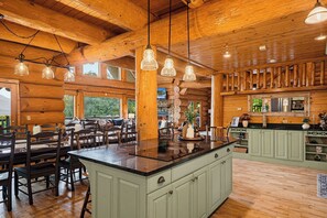 A log cabin interior with a central island, dining area, kitchen, and large windows. - Round Log Cabin with Stunning Views (Gatlinburg)