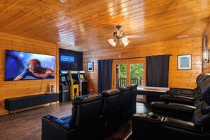A room with a large flat-screen TV, gaming consoles, a ceiling fan, and leather seating. - Round Log Cabin with Stunning Views (Gatlinburg)