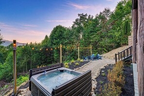 A hot tub surrounded by a wooden deck, with a stone pathway leading to outdoor seating. - Round Log Cabin with Stunning Views (Gatlinburg)