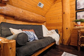 A cozy log cabin interior with a wooden sofa, pillows, and a small table with a plant.