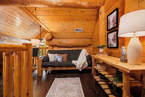 A cozy log cabin interior with a sofa, a table with a lamp, and a fireplace.