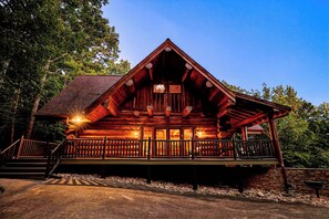 A log cabin with a porch, a staircase, and a stone wall. - Round Log Cabin with Stunning Views (Gatlinburg)