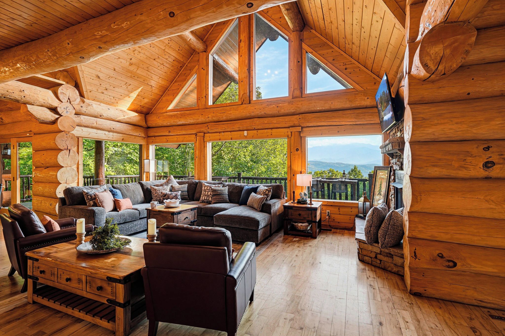A log cabin interior with a large sofa, a coffee table, and a television mounted on the wall.