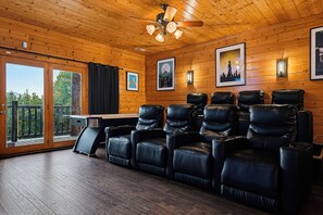 Een kamer met een houten plafond, een plafondventilator, een groot raam met gordijnen, een zithoek met leren stoelen en lijstwerken aan de muur.