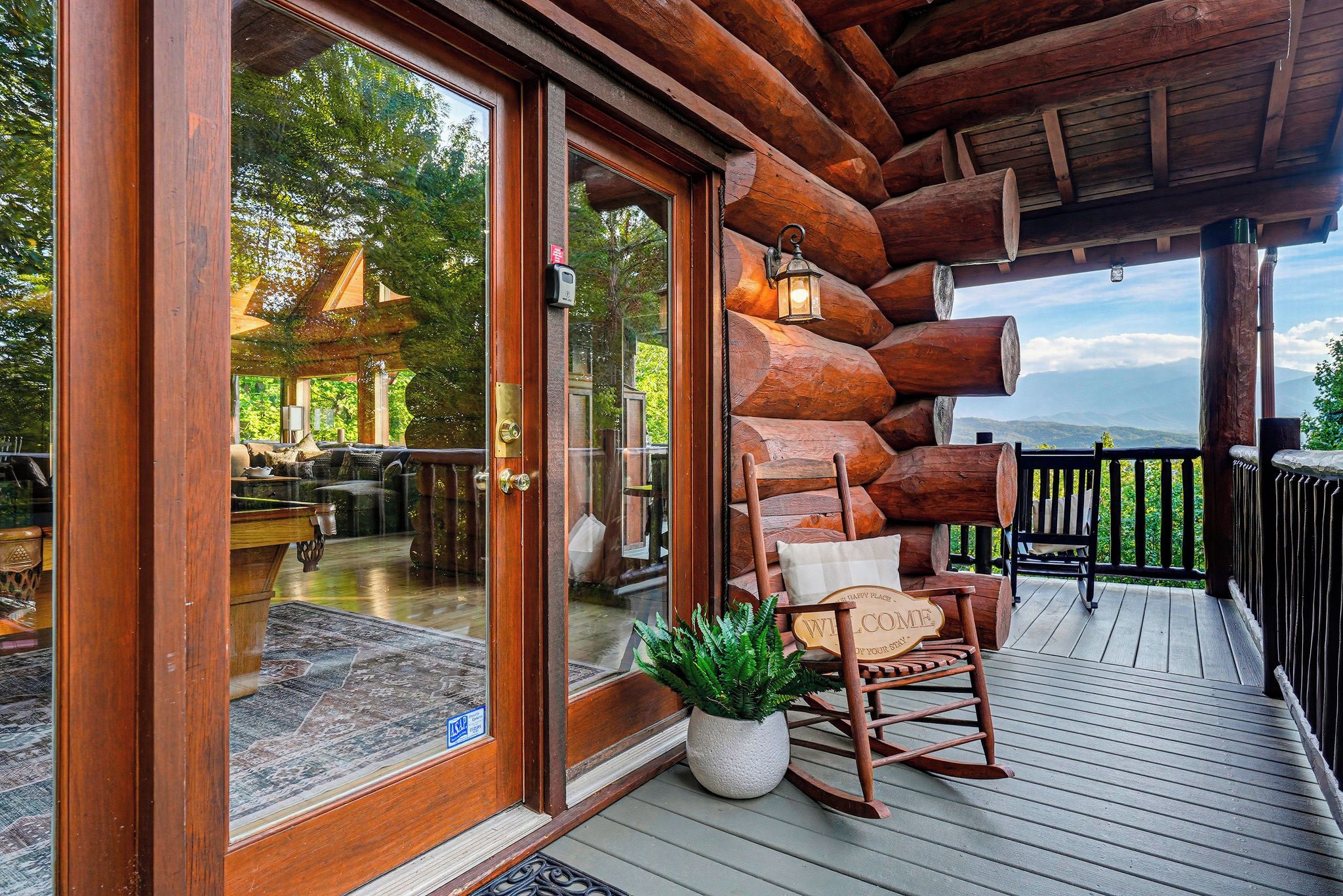 Une terrasse en bois avec un fauteuil à bascule et une pancarte de bienvenue, offrant une vue sur un paysage montagneux.