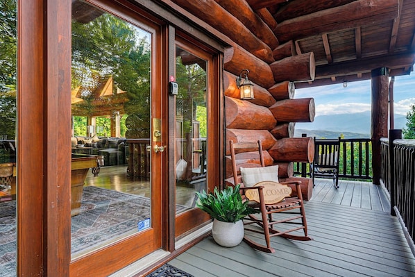 A wooden deck with a rocking chair and a welcome sign, overlooking a mountainous landscape.