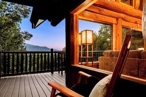 Eine Holzdielen-Terrasse mit Blick auf Berge, eine Bank und ein Tisch mit einer Lampe.