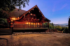 A wooden cabin with a porch, a stone wall, and a gravel driveway. - Round Log Cabin with Stunning Views (Gatlinburg)