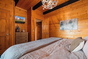 A wooden cabin bedroom with a bed, dresser, and artwork on the wall.