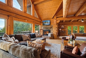A spacious log cabin interior with a fireplace, comfortable seating, and large windows.