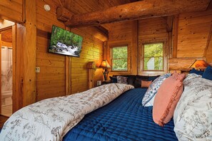A wooden cabin room with a bed, a television, and a window. - Round Log Cabin with Stunning Views (Gatlinburg)