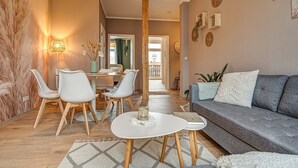 Un salon moderne avec un canapé gris, des chaises blanches, une petite table blanche et un coin repas comprenant une table et des chaises.