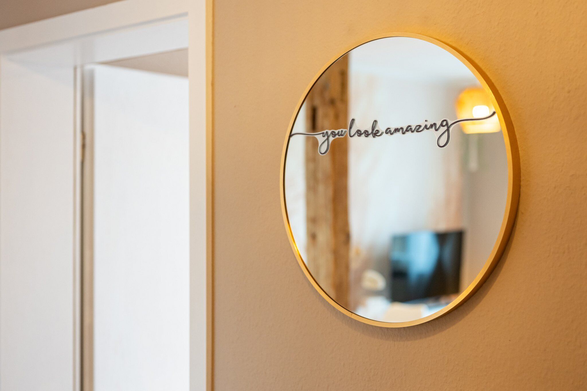 Een ronde spiegel met een gouden lijst aan een beige muur.