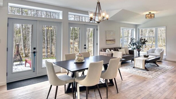 A spacious living room with a large dining table, comfortable seating, and large windows offering a view of the outdoors. - 1 month for the price of 1 week! (Mont-Tremblant)