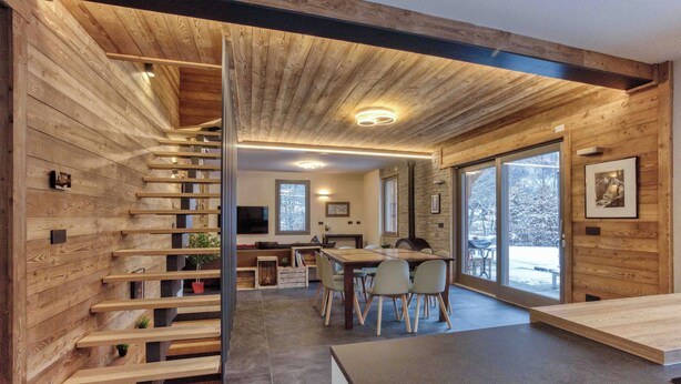 A modern interior with a wooden staircase, a dining area with chairs, and a kitchen with a large window. - Chalet Verney. Family chalet near Chamonix center (Chamonix-Mont-Blanc)