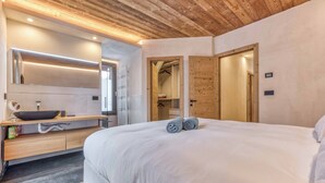 A modern bedroom with a large bed, wooden ceiling, and a built-in vanity with a mirror and sink. - Chalet Verney. Family chalet near Chamonix center (Chamonix-Mont-Blanc)