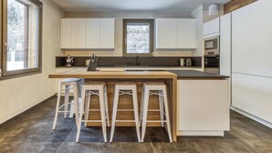 A modern kitchen with a central island, white bar stools, and built-in appliances. - Chalet Verney. Family chalet near Chamonix center (Chamonix-Mont-Blanc)