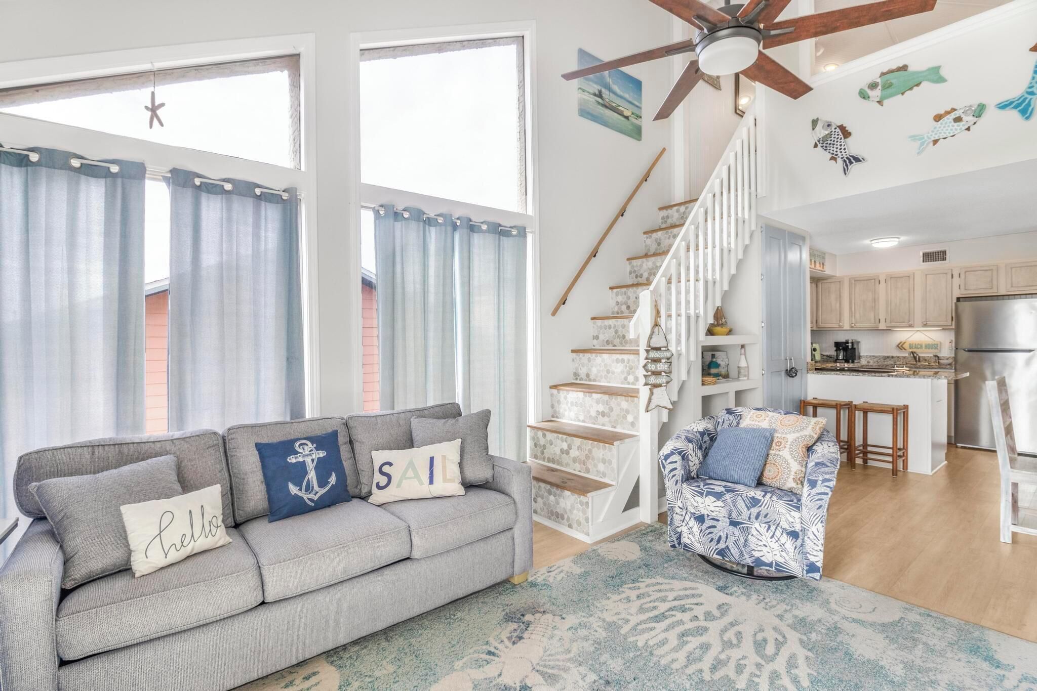 A living room with a grey sofa, patterned armchair, and a staircase leading to a kitchen.