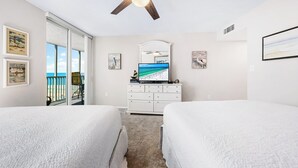 A hotel room with two beds, a ceiling fan, a large window with a view of the beach, and a dresser with a flat-screen TV. - Stunning Sunsets! 2 Bed, 2 Bath Condo on Siesta Key! (Siesta Key)